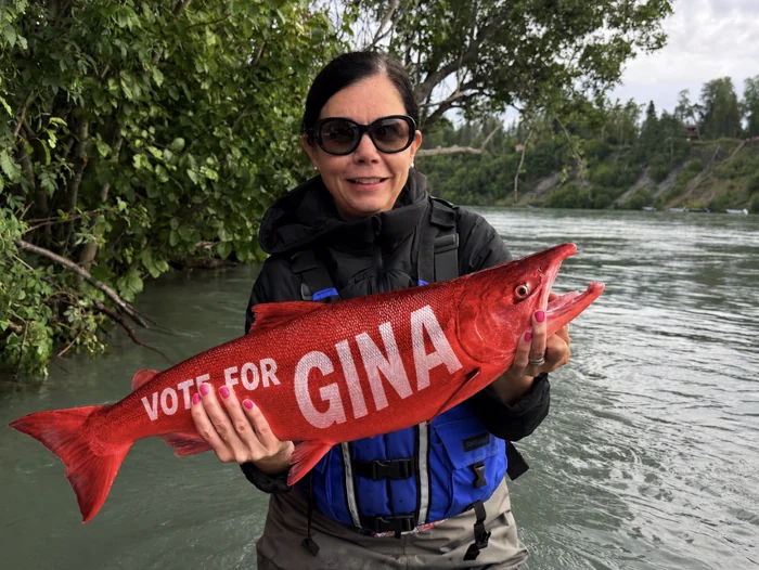 Gina Wall on the Kenai River holding a salmon painted with Vote for Gina
